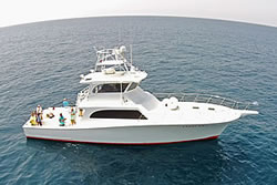 ladyem-glamour-shot-1 A white yacht with a red stripe is floating on calm blue ocean water. Several people are on the deck, enjoying the view and relaxing under partly cloudy skies.
