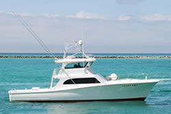 ladyem-glamour-shot-4 A white sport fishing boat with a cabin and upper deck is floating on calm turquoise water near a distant breakwater under a partly cloudy sky.